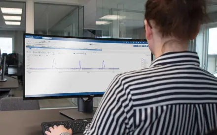 Person monitoring real-time temperature data on a computer screen using a cold chain tracking dashboard in an office setting.